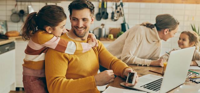 Happy daughter embracing her father who is working on laptop at home
